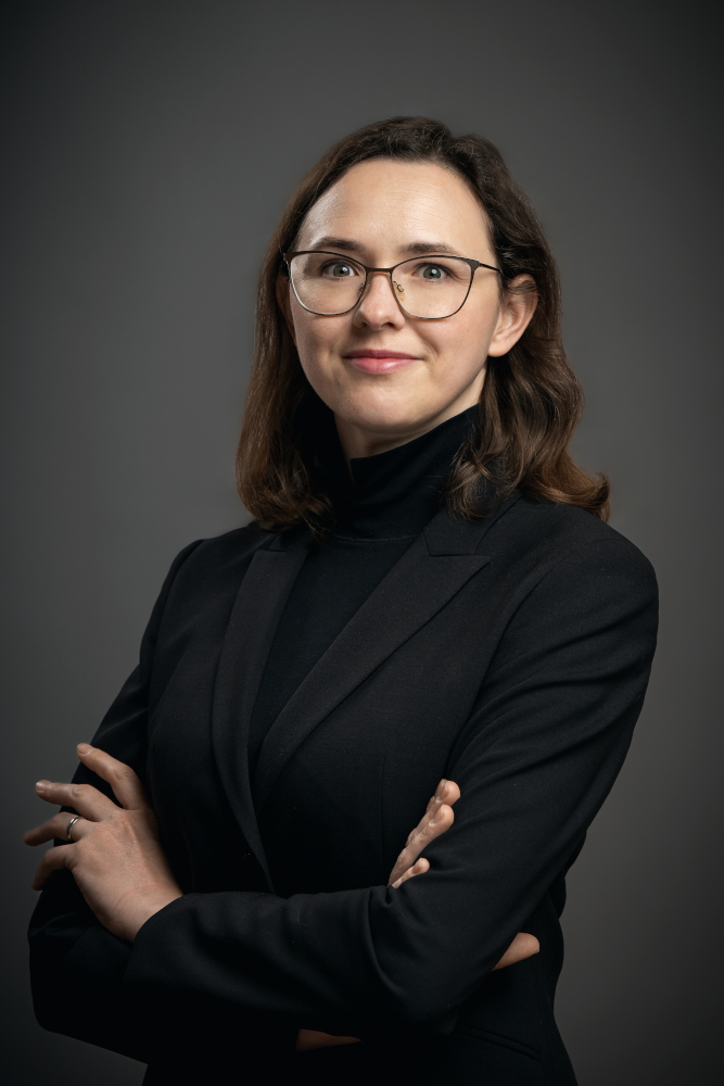 A picture of Anna Prysłopska in a black blazer on a gray background.